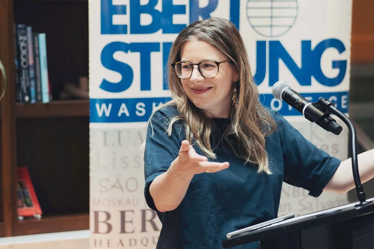 Jordan Leichnitz (FES Canada Country Director) speaks at FES event, gesturing at podium with FES banner and bookshelves behind.