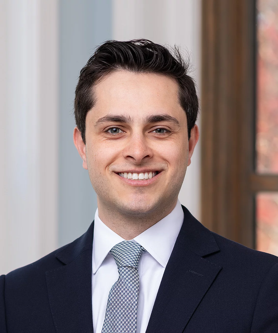 young man with dark hair in a suit smiling