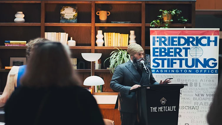 Jagmeet Singh (former leader of the New Democratic Party) in gray suit and turban speaks at podium with Friedrich-Ebert-Stiftung Buenos Aires banner in wood-paneled room with plants and ceramics. 