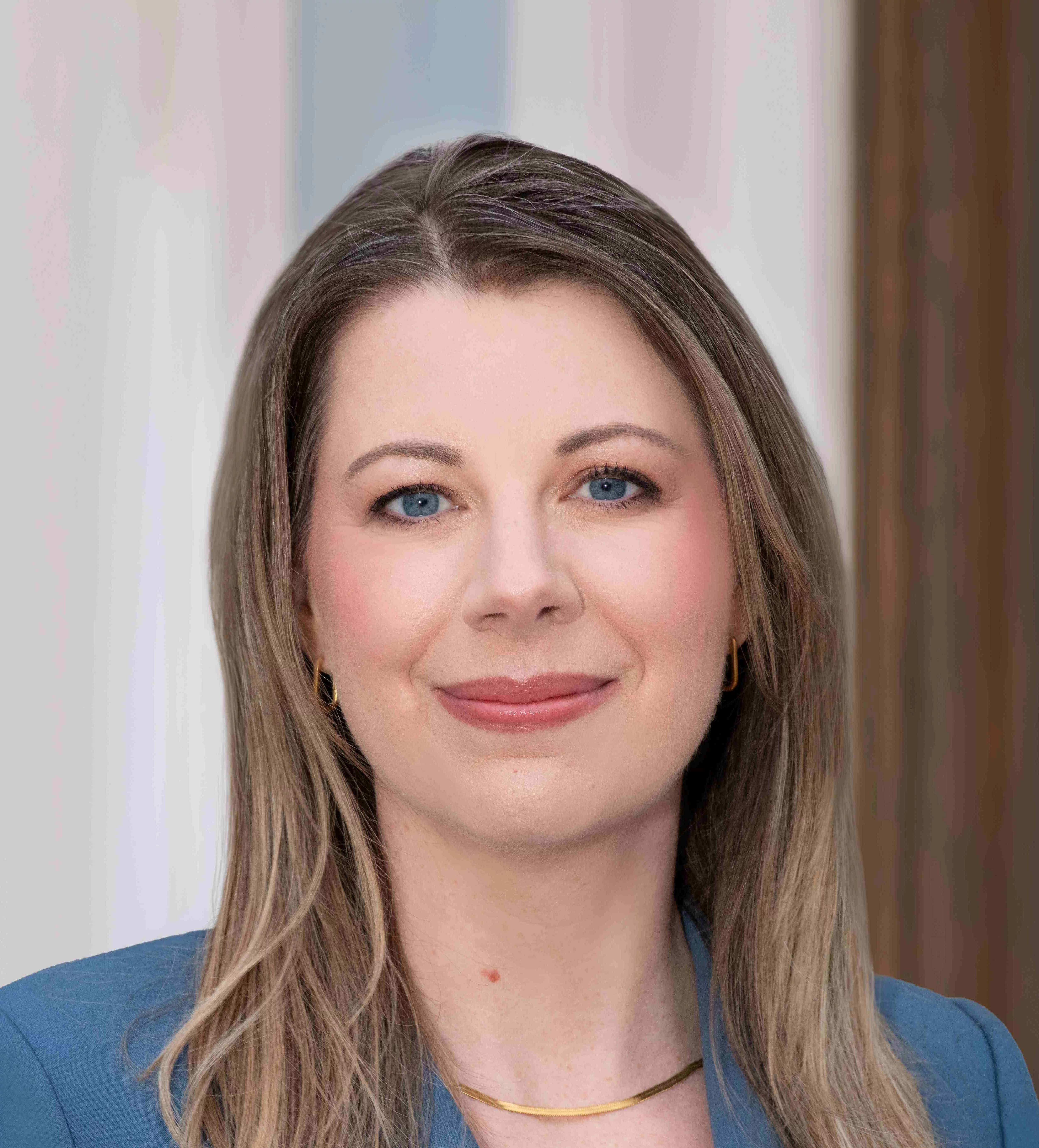 woman with dark blonde hair in a light blue suit smiling