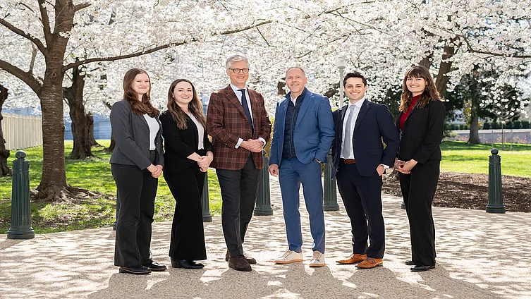 six colleagues in business attire standing in front of cherry blossom trees
