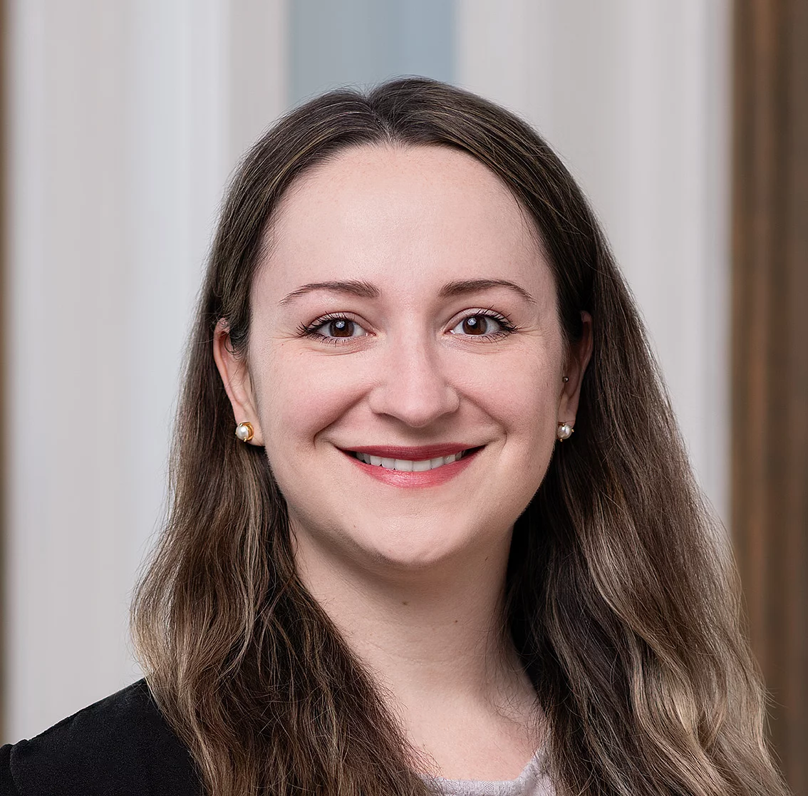 young woman with brown hair wearing a suit smiling into the camera